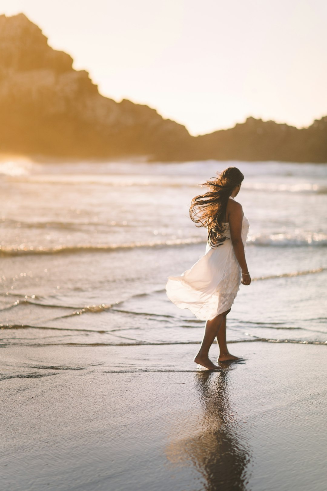 Photo by Saksham Gangwar selective focus photo of woman standing on sea shore near rock formation during golden hour