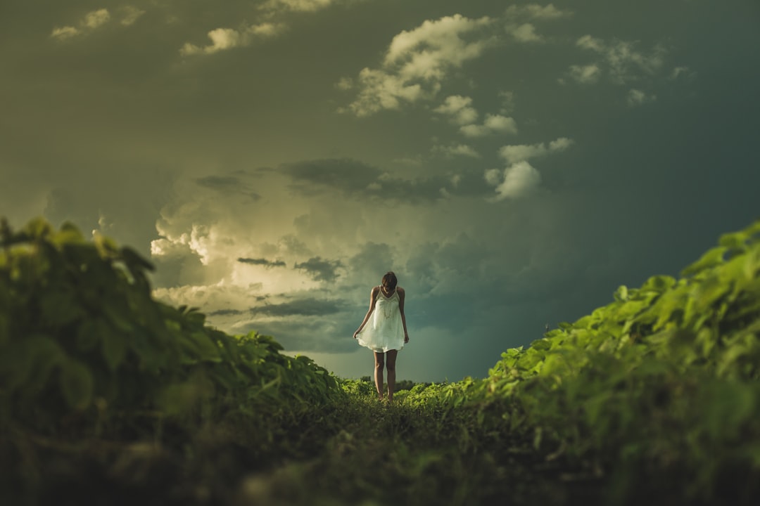 Photo by Matthew Henry woman wearing white dress standing on hill with green grass under white cloudy sky